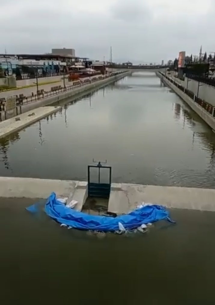 Wehrbereich des Kanals in Avlu; die Wasseroberfläche ist trüb, um das Wehr liegt eine blaue Plane